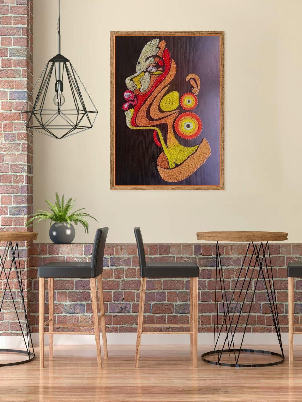 Tableau abstrait encadré d'un visage de profil en fils orange, rouge et jaune accroché à un mur