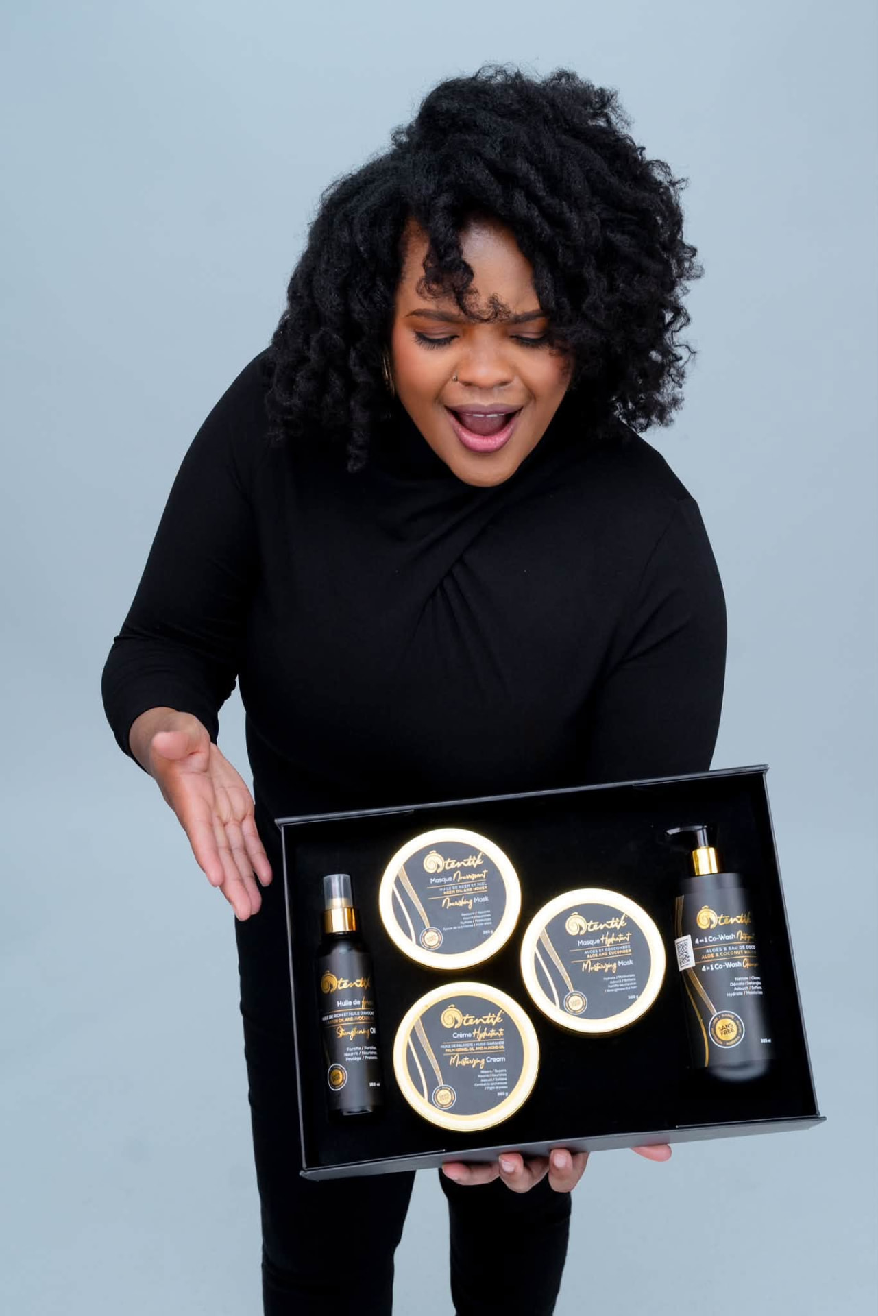Femme aux cheveux naturels présentant le coffret Ôtentik avec masques, crème hydratante, huile et co-wash