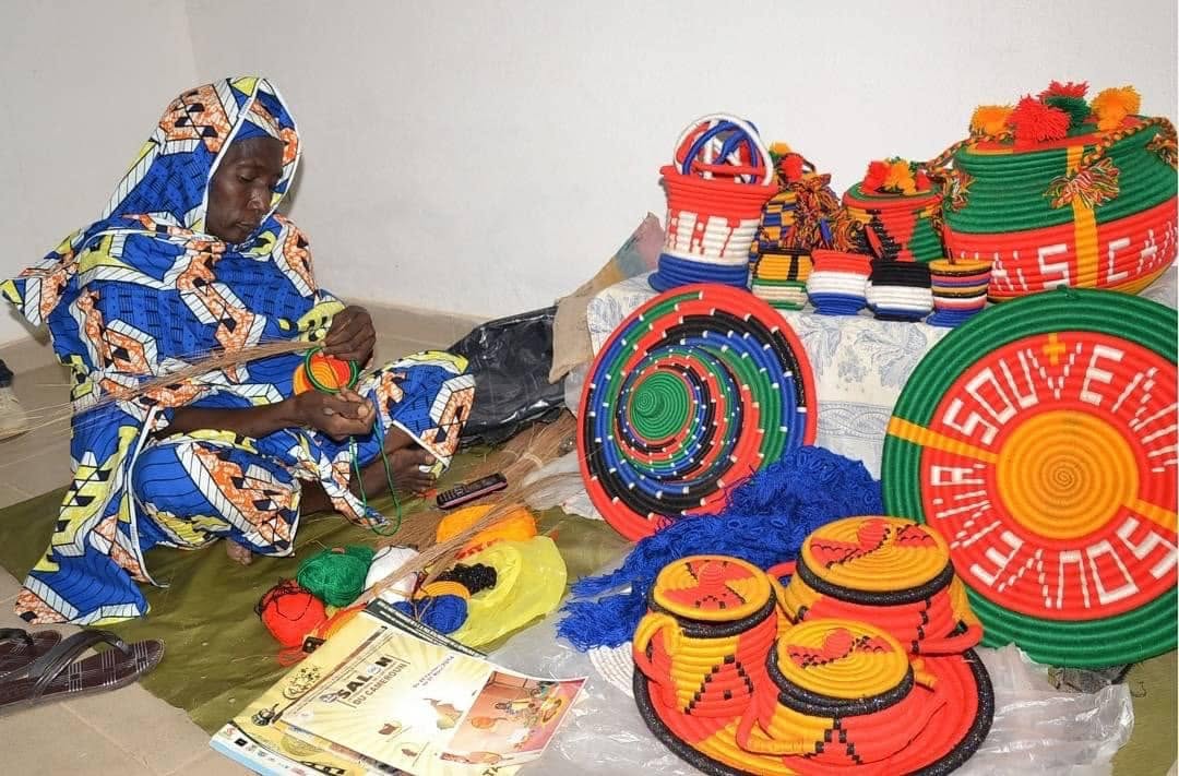 Artisane confectionnant des paniers et plateaux colorés au Village Artisanal de Garoua
