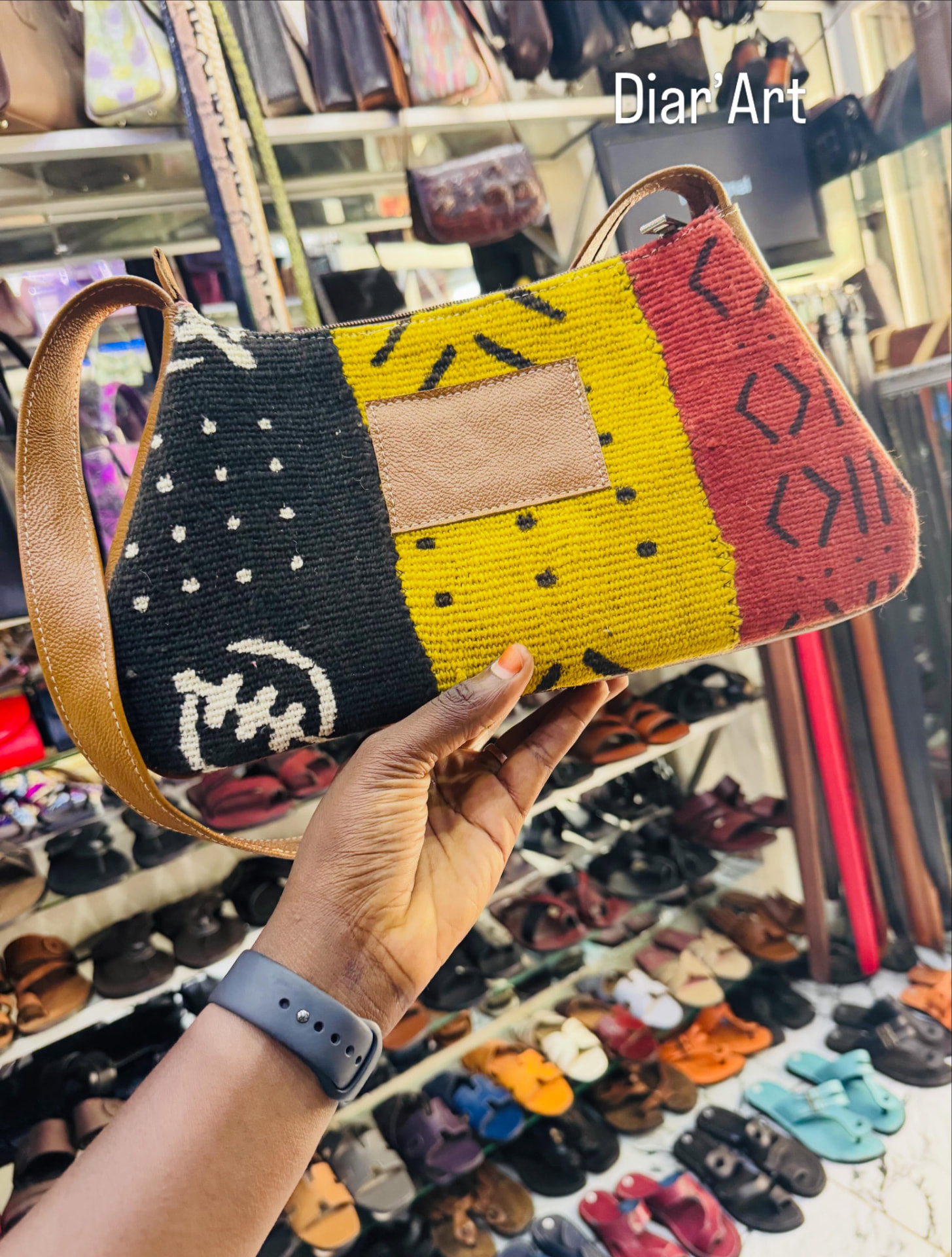 Sac tricolore en tissu bogolan et cuir tenu en main dans la boutique