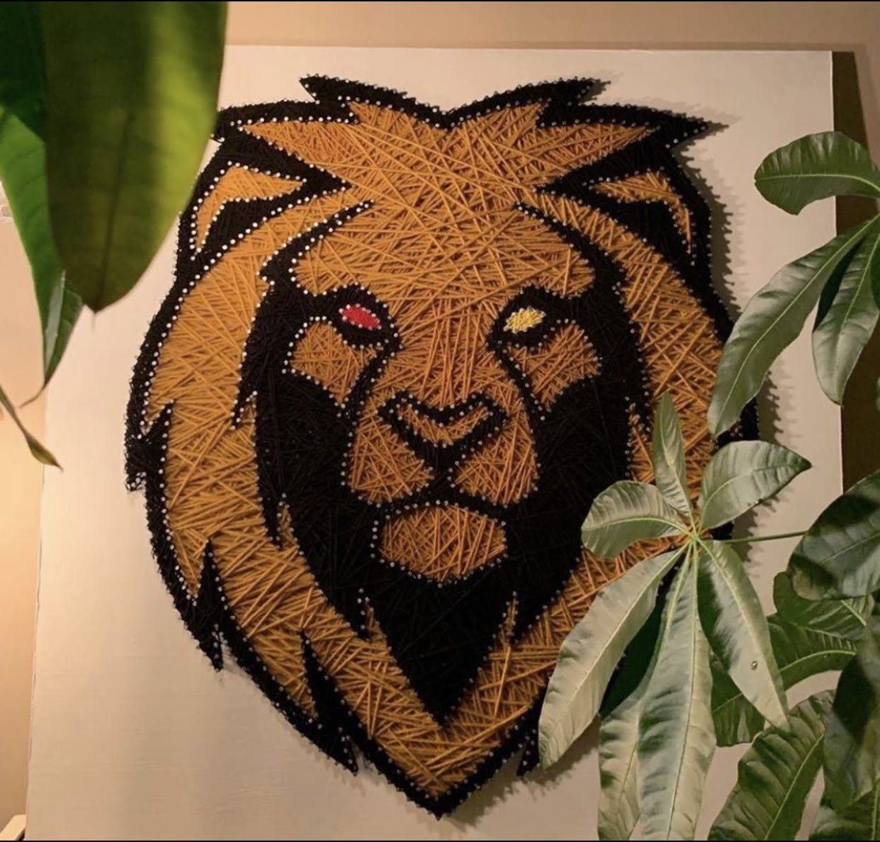 Grande tête de lion réalisée en fils dorés et noirs sur panneau blanc