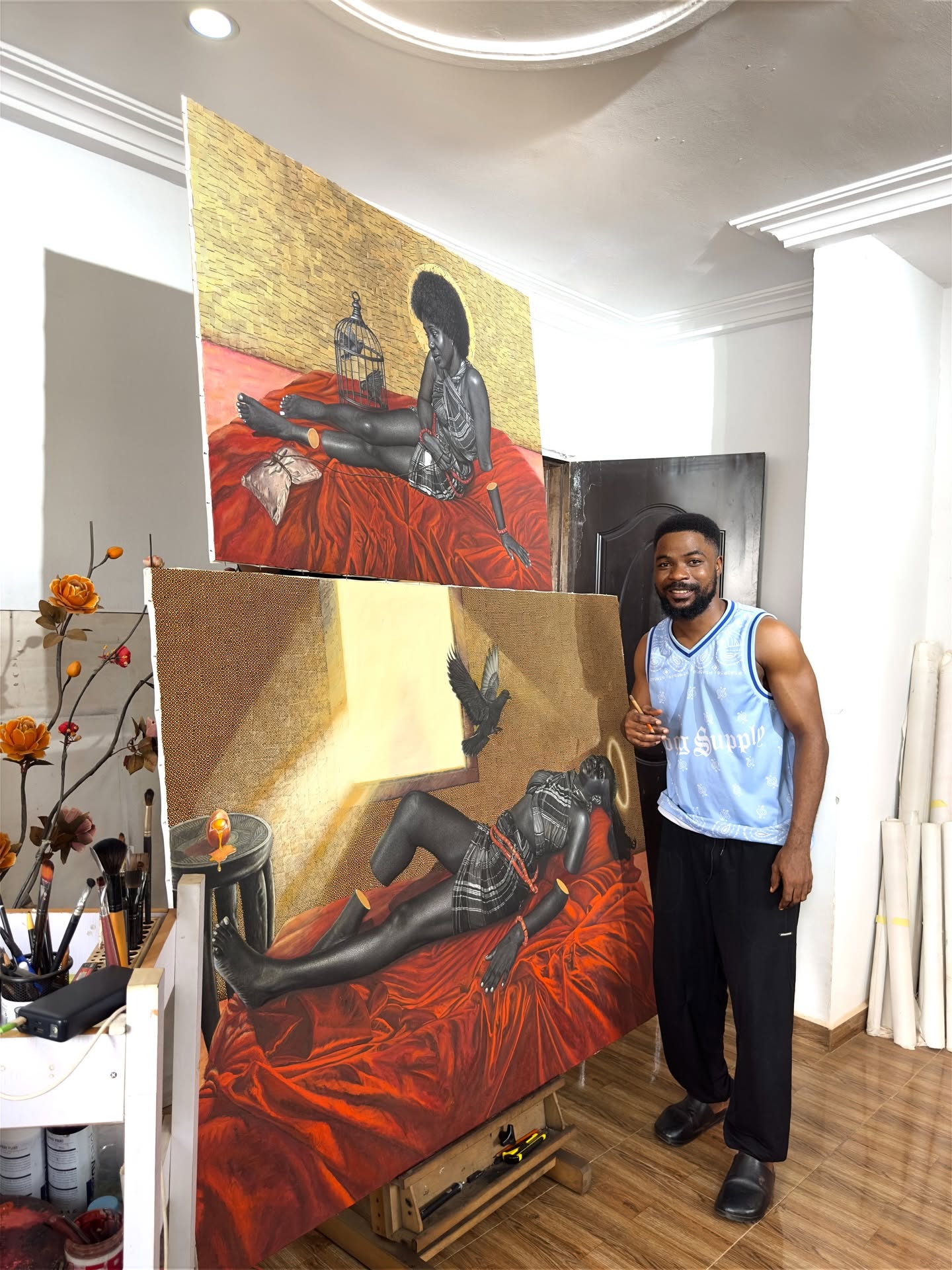 Hopex John souriant à côté de deux œuvres sur drapé rouge et fond doré